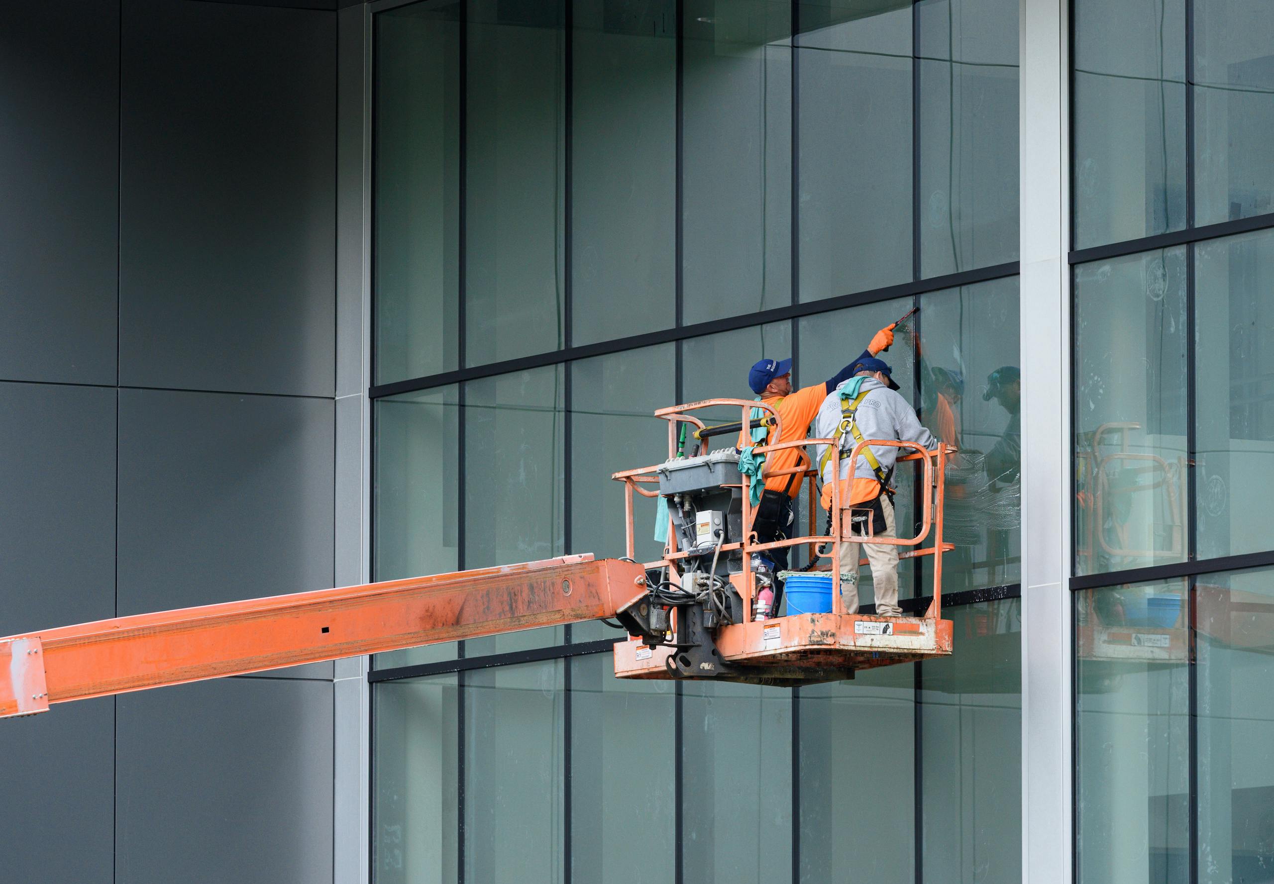 Workers on a lift platform cleaning glass windows of a modern high-rise building safely.